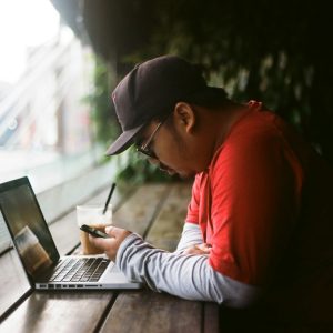 man holding phone in with laptop beside cup