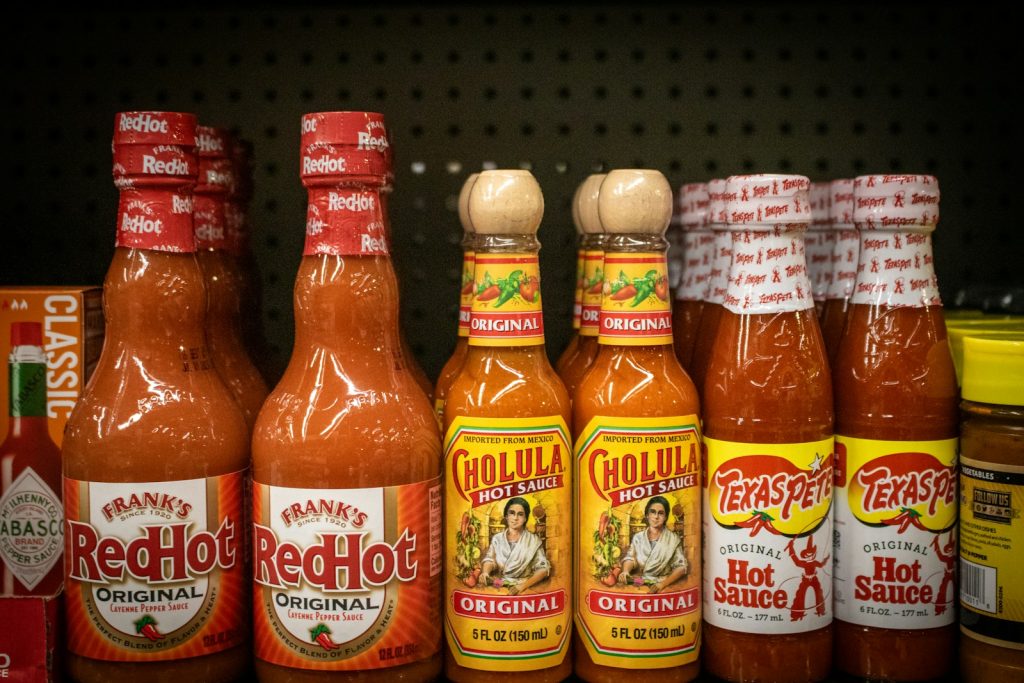 Shelf displays various bottles of hot sauce.