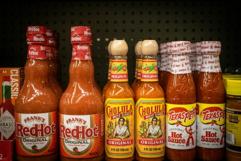 Shelf displays various bottles of hot sauce.